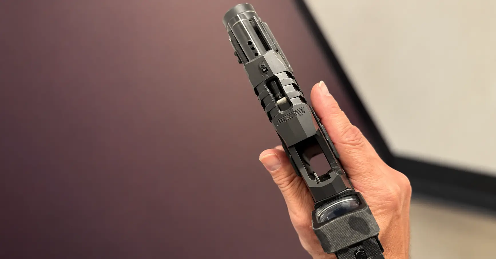 Close-up of a handgun held with the index finger straight along the frame, outside the trigger guard.